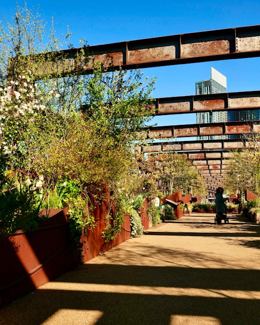 A vibrant urban garden scene featuring diverse plantings of purple, yellow, and green foliage in a landscaped bed. The garden includes a variety of flowering plants and ornamental grasses with texture